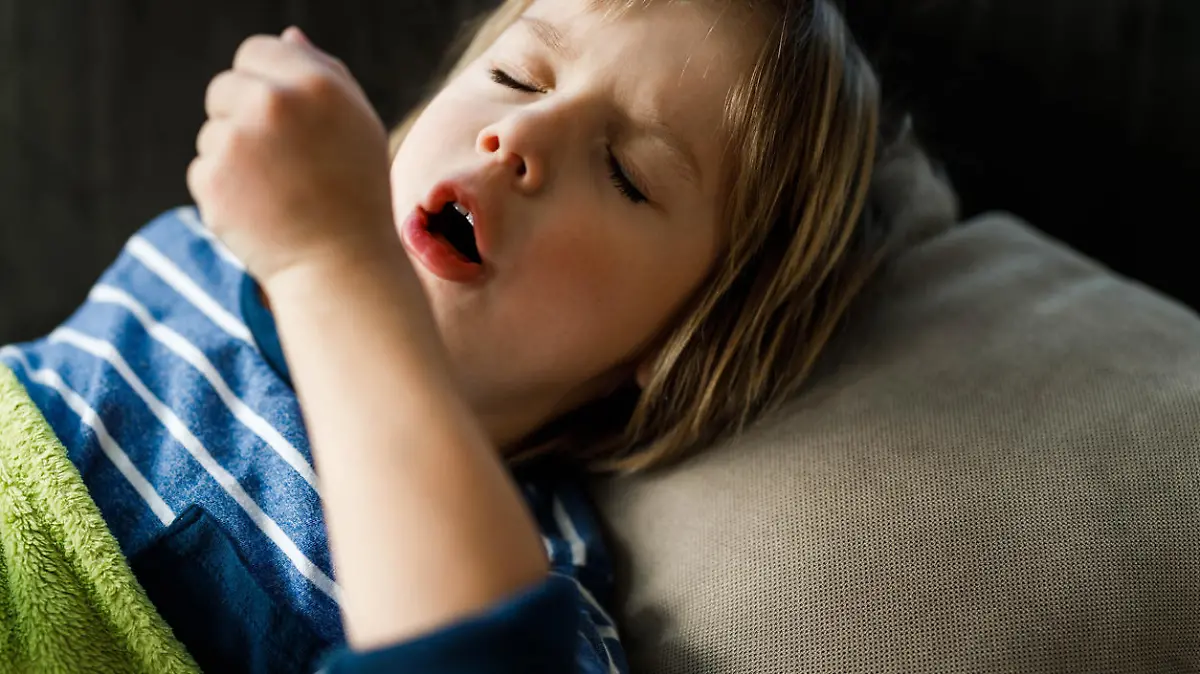 Little ill boy coughing while having a virus in bed at home.