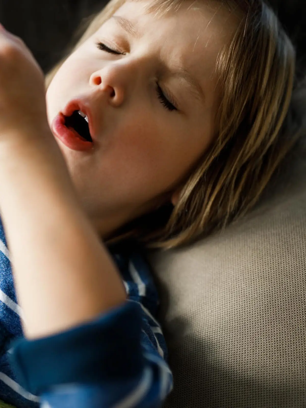 Little ill boy coughing while having a virus in bed at home.