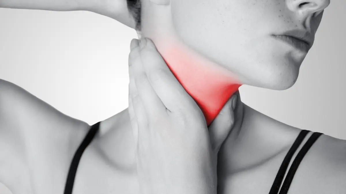 Closeup view of a young woman with pain on neck or thyroid gland on gray background. Black and white photo with red dot. || Modellfreigabe vorhanden