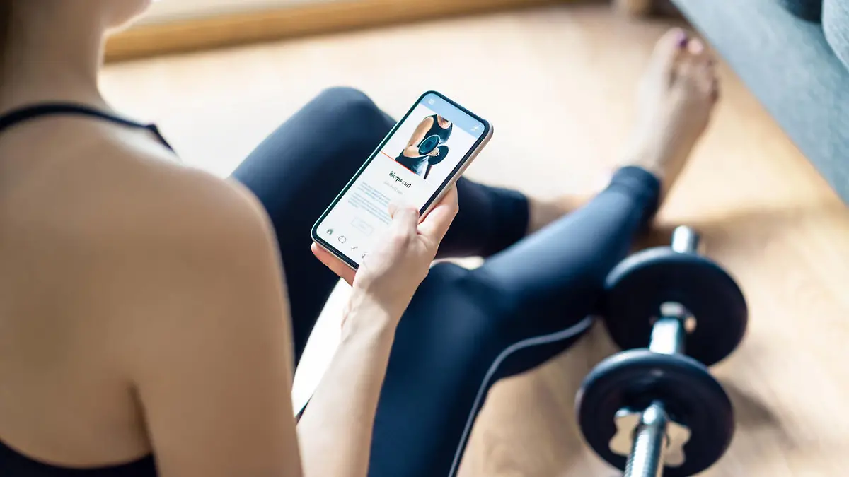 Home gym workout with online exercise app in phone. Fit woman watching training tutorial video or using digital personal trainer with smartphone. Internet coach. Sport routine or class in cellphone.
