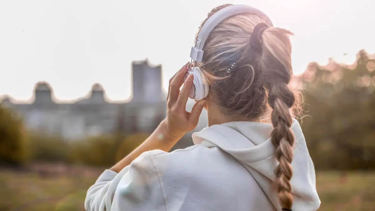 Beautiful blonde woman listening to music in a public park after a fitness training with city in background and hold tablet.