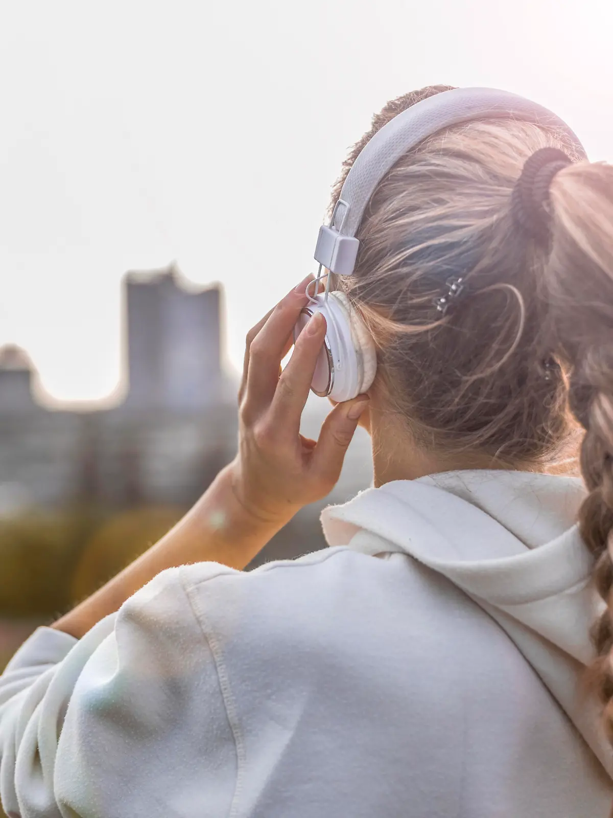 Beautiful blonde woman listening to music in a public park after a fitness training with city in background and hold tablet.