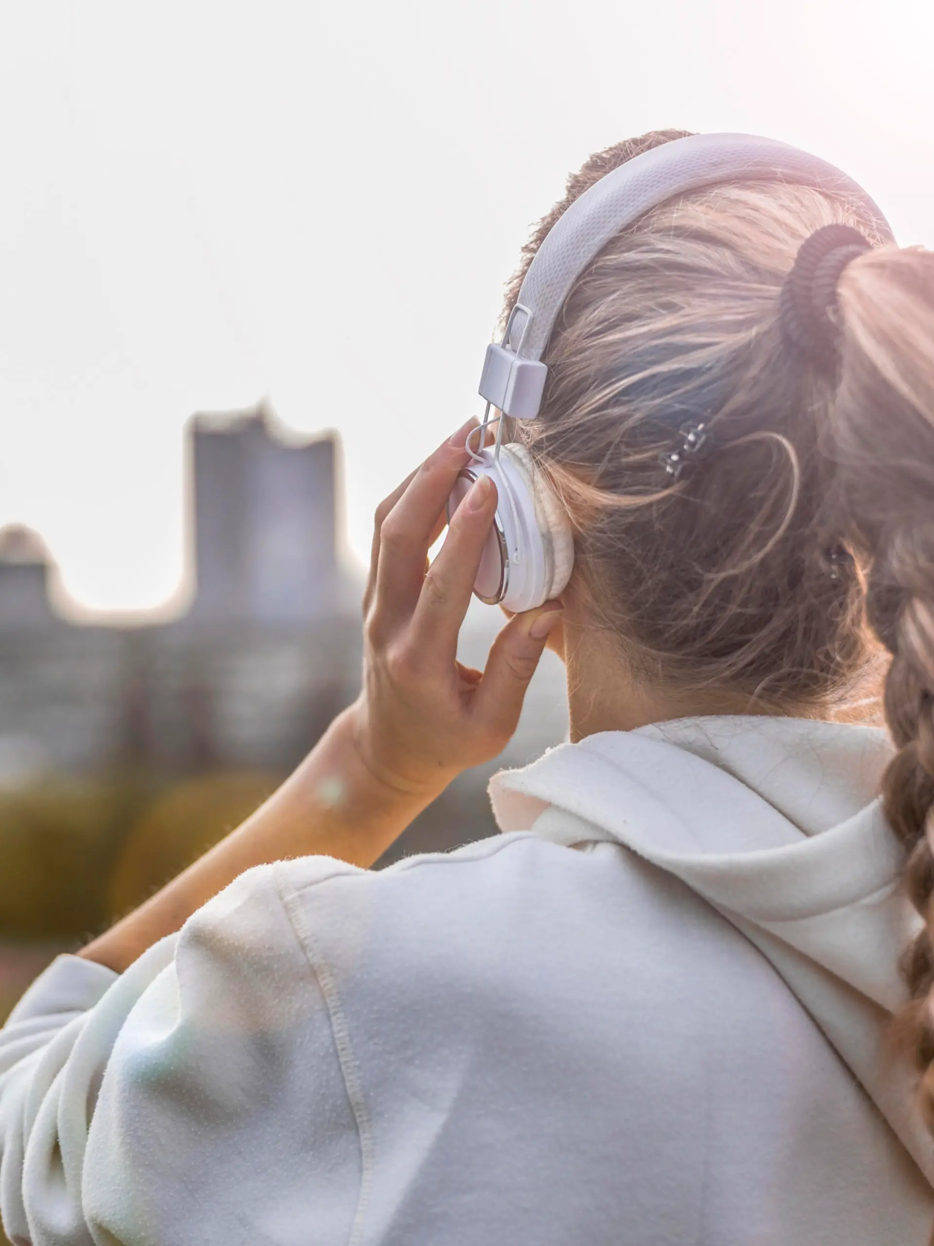 Beautiful blonde woman listening to music in a public park after a fitness training with city in background and hold tablet.