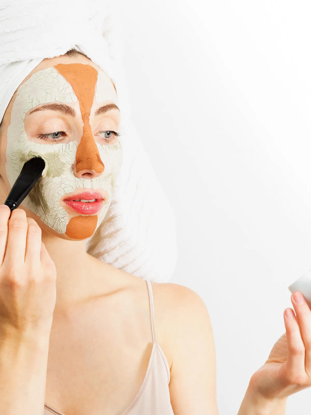 Beauty procedures skin care concept. Young woman applying facial gray and red mud clay mask to her face in bathroom. Woman with different masks on her face multi-masking