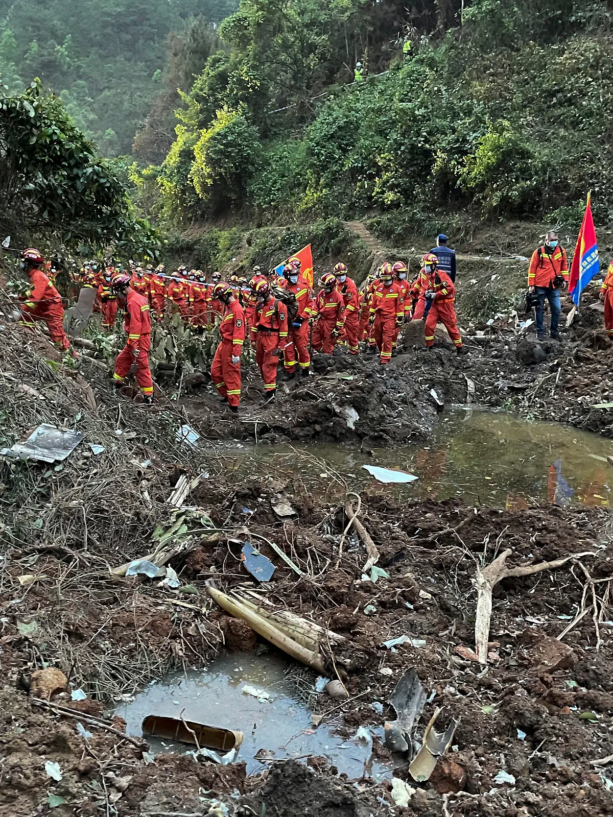 In this photo released by Xinhua News Agency, rescuers conduct search operations at the site of a plane crash in Tengxian County in southern China's Guangxi Zhuang Autonomous Region, Tuesday, March 22, 2022. Mud-stained wallets. Bank cards. Official identity cards. Some of the personal effects of 132 lives presumed lost were lined up by rescue workers scouring a remote mountainside Tuesday for the wreckage of a China Eastern plane that one day earlier inexplicably fell from the sky and burst into a huge fireball. (Zhou Hua/Xinhua via AP)
