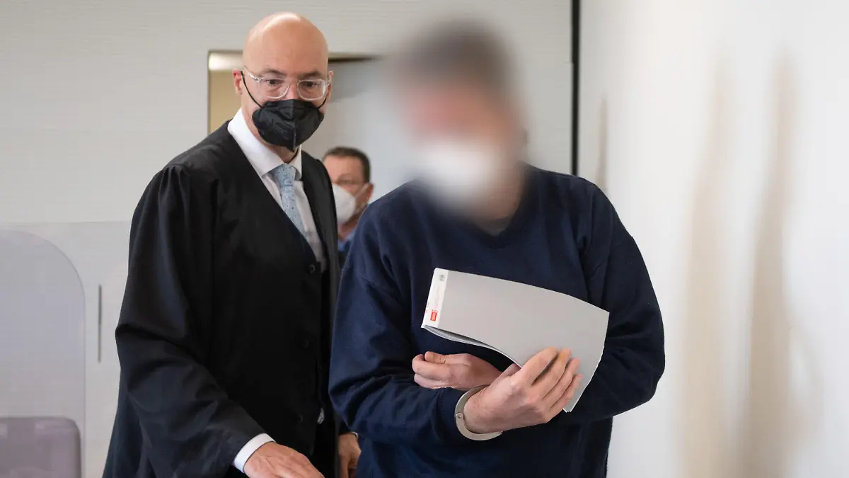 21.03.2022, Rheinland-Pfalz, Bad Kreuznach: Der Angeklagte wird in Handschellen in den Gerichtssaal gebracht. Links sein Anwalt Alexander Klein. Der Mann soll im vergangenen Jahr in Bad Kreuznach den Mitarbeiter einer Tankstelle erschossen haben, nachdem dieser ihn auf die coronabedingte Maskenpflicht hingewiesen hatte. Foto: Boris Roessler/dpa - ACHTUNG: Der Angeklagte wurde auf Anordnung des Gerichts gepixelt +++ dpa-Bildfunk +++