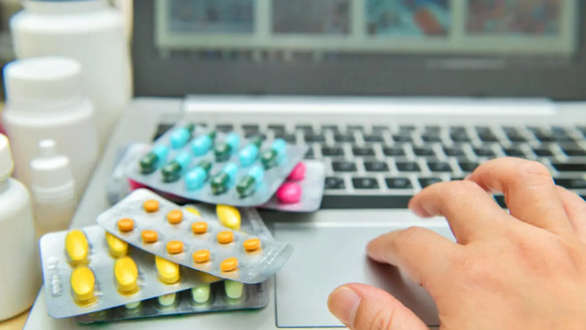 Pills, blister packs and medical bottles in front of laptop. Health care and internet shopping.