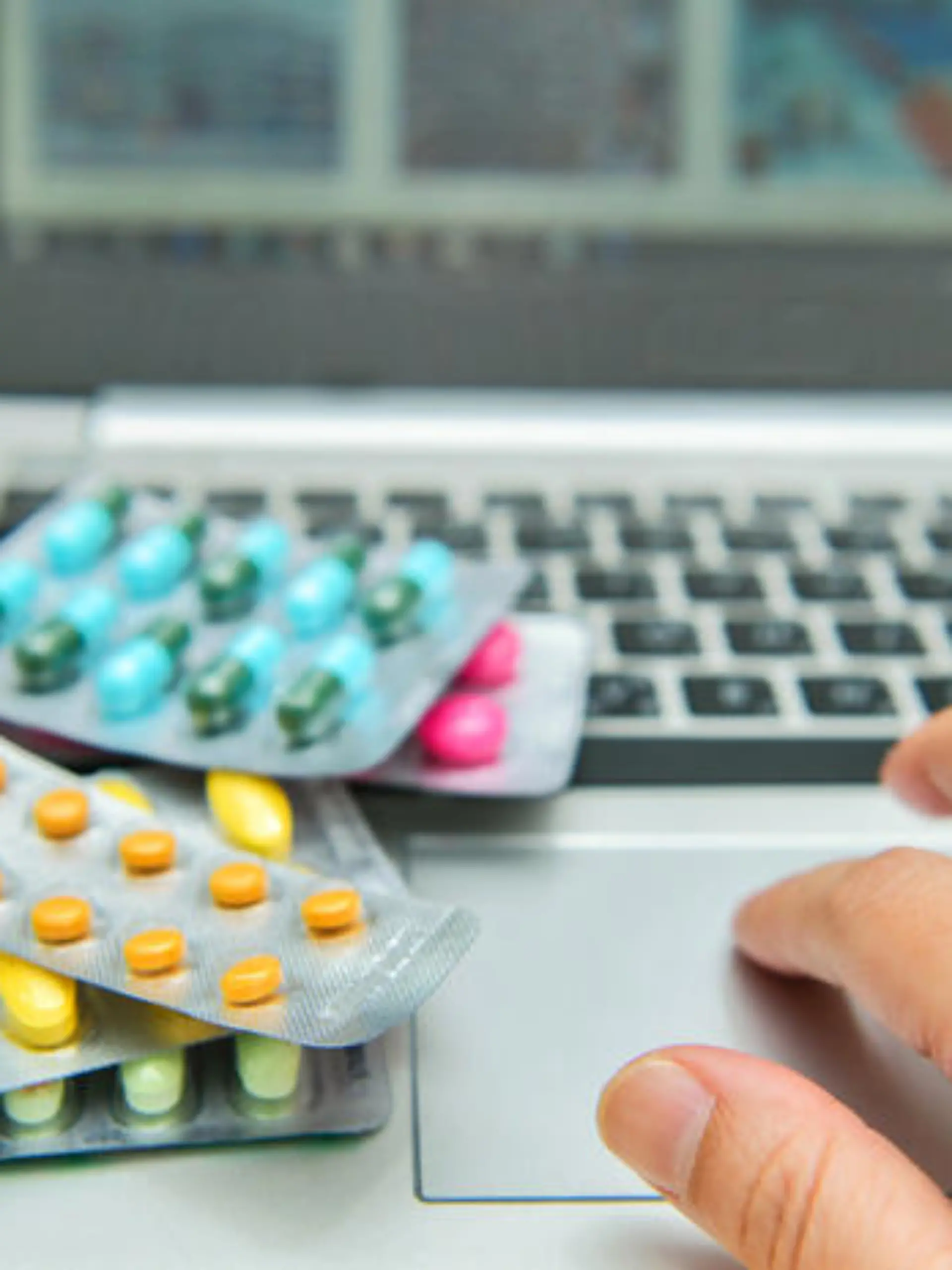 Pills, blister packs and medical bottles in front of laptop. Health care and internet shopping.