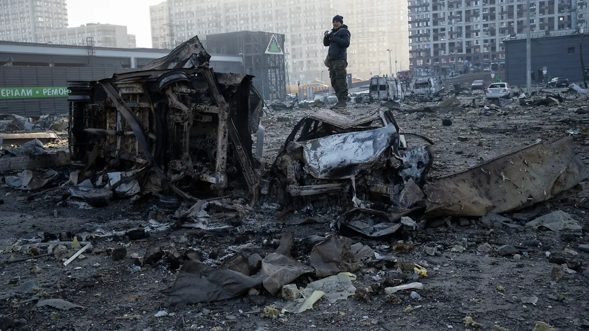 21.03.2022, Ukraine, Kiew: Ein Mann steht auf einem Autowrack inmitten der Zerstörung, die nach dem Beschuss eines Einkaufszentrums in Kiew entstanden ist. Foto: Rodrigo Abd/AP/dpa +++ dpa-Bildfunk +++