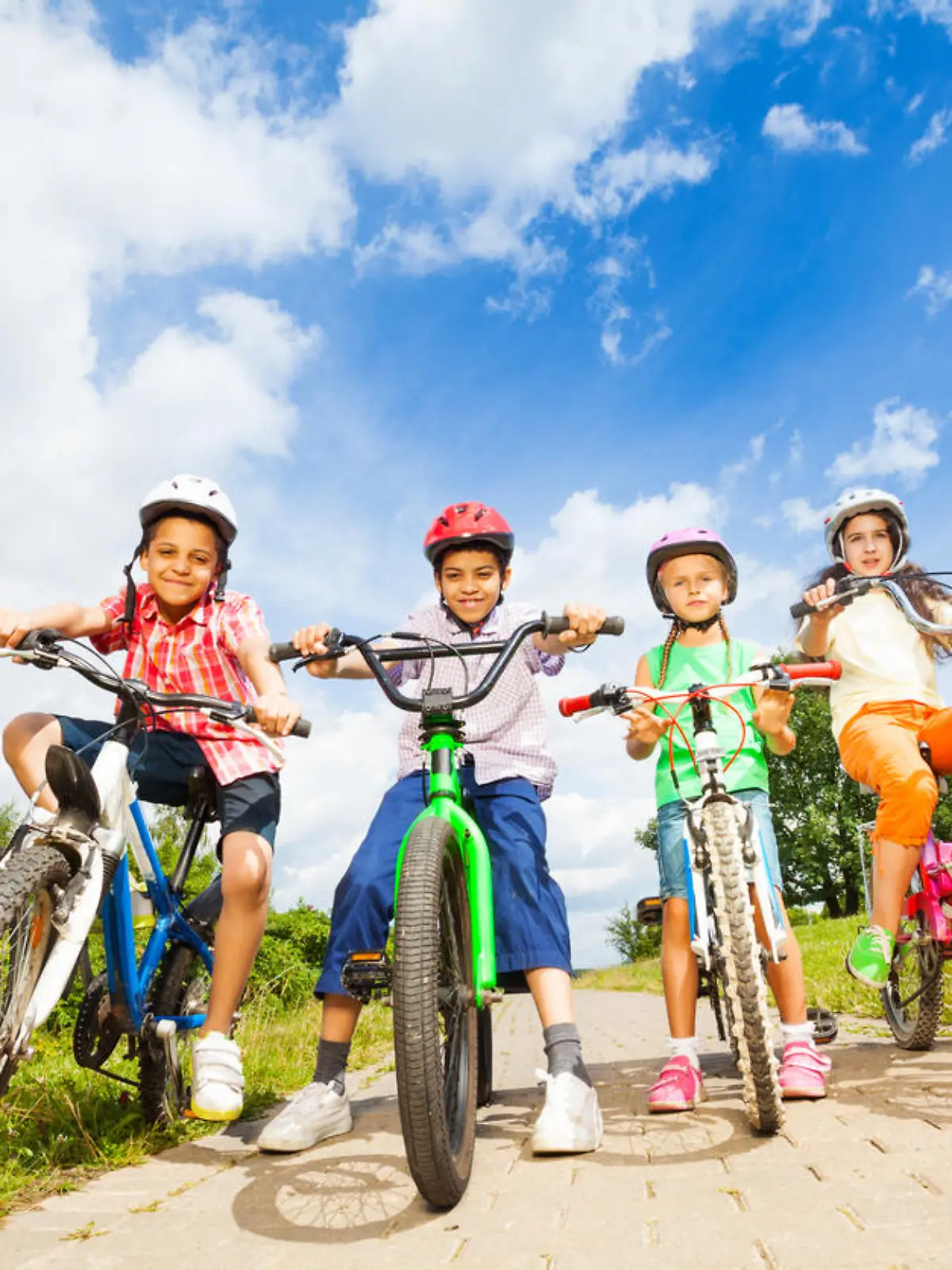Below angle view of kids in helmets who hold their bikes and stand on path
