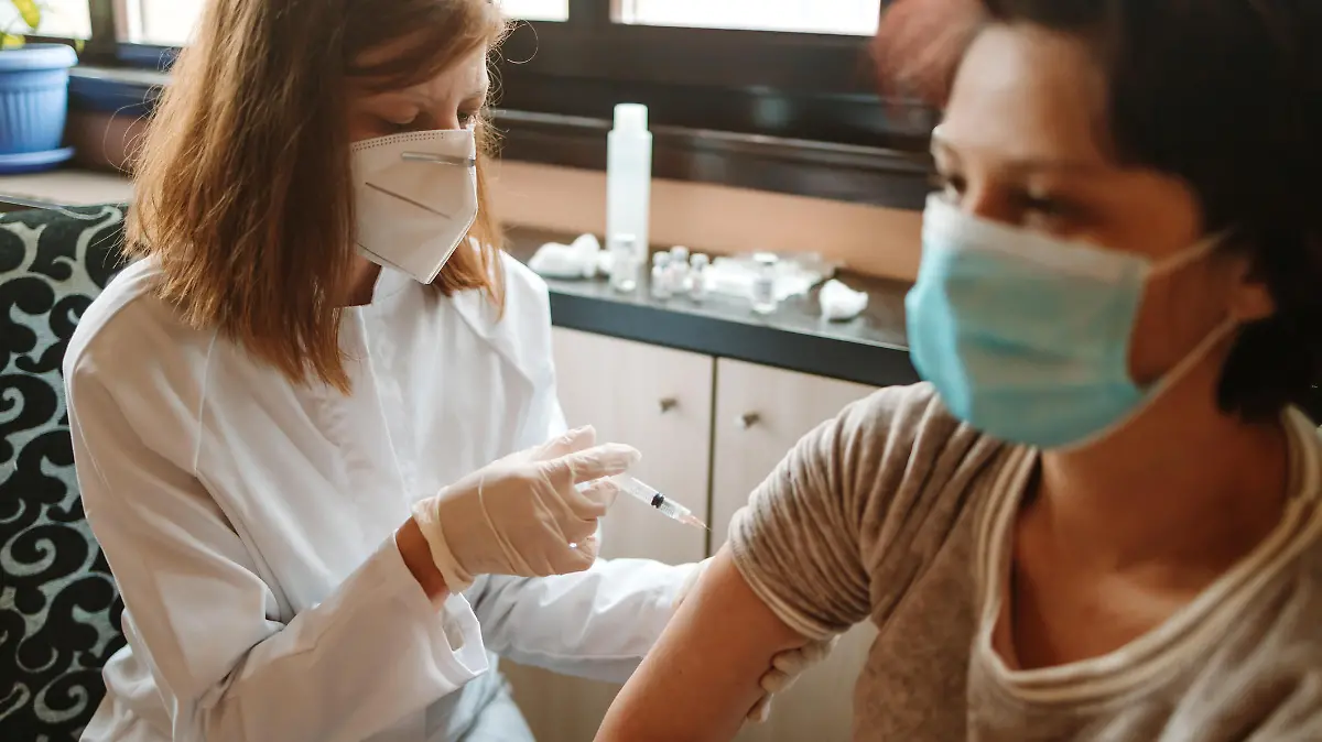 Mature woman getting a COVID-19 vaccine by a female nursing doctor at home