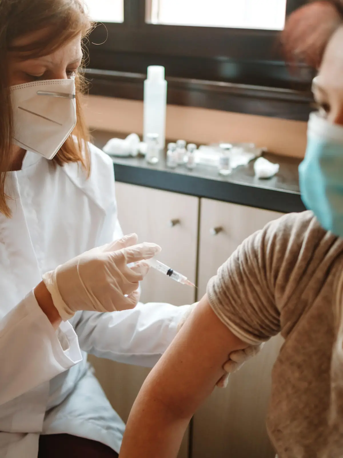 Mature woman getting a COVID-19 vaccine by a female nursing doctor at home