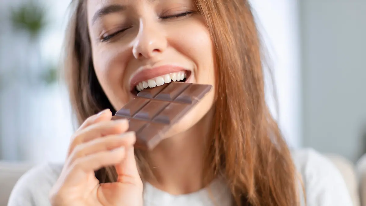 Cheerful young woman eating chocolate at home