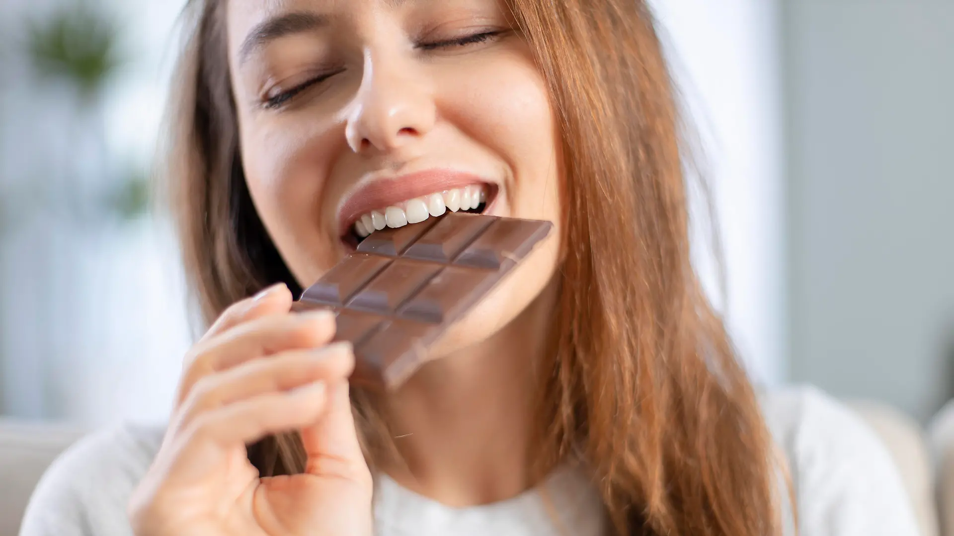 Cheerful young woman eating chocolate at home