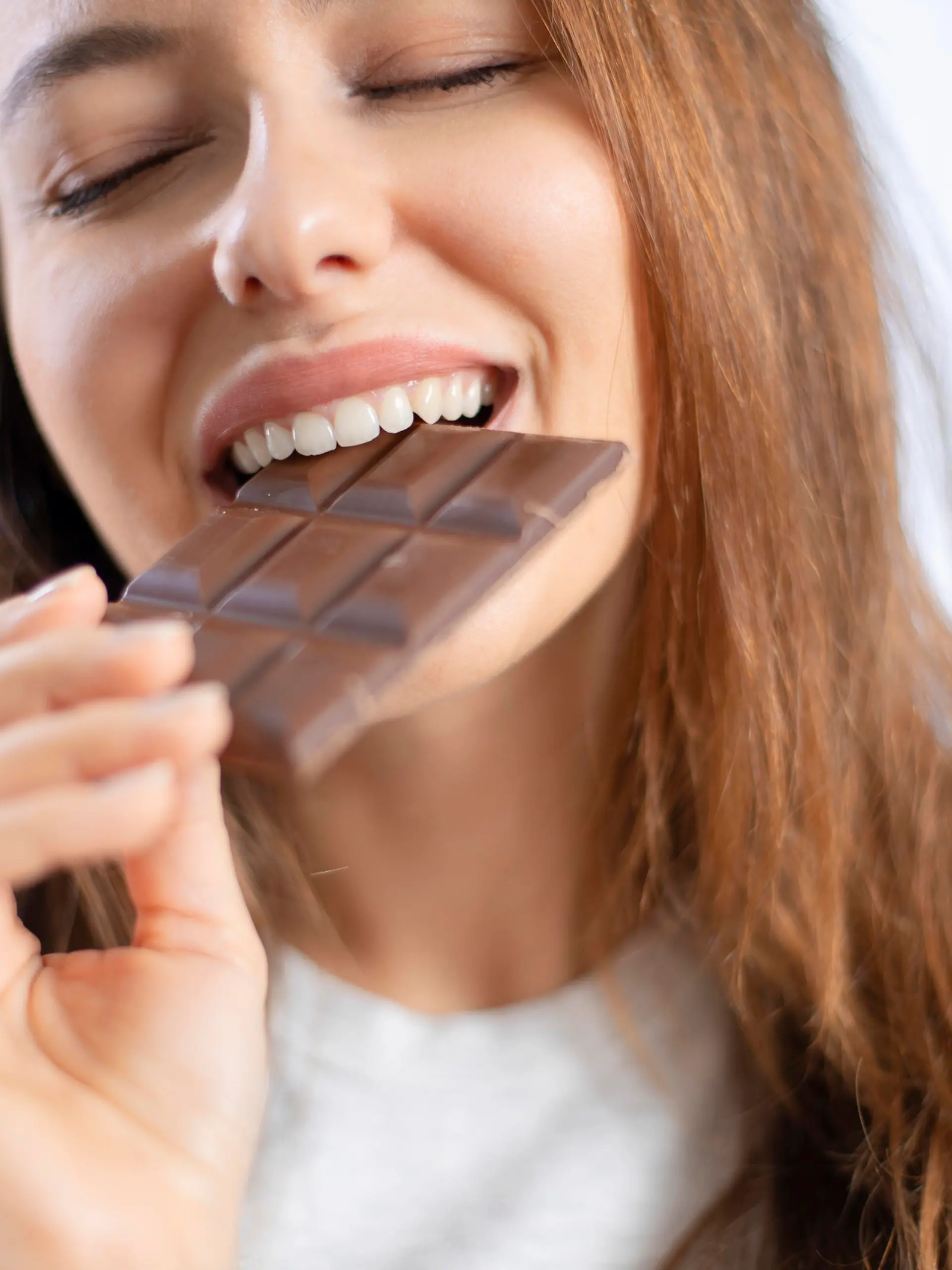Cheerful young woman eating chocolate at home