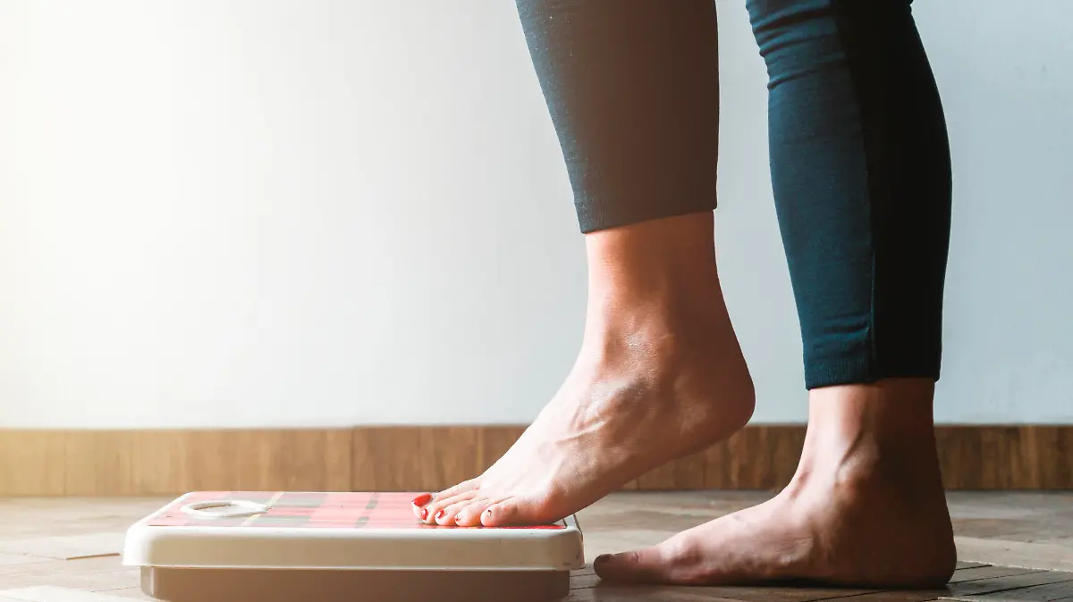 Female checking kilogrammes getting on the scale - self care and body positivity concept - warm flare on left