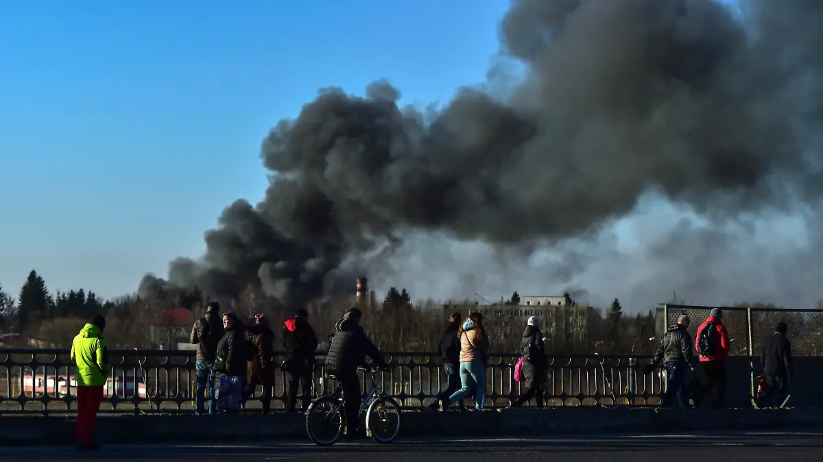 18.03.2022, Ukraine, Lwiw: Menschen stehen auf einer Überführung und schauen auf eine Rauchwolke, die nach einer Explosion in der Nähe des Flughafens aufsteigt. Am Flughafen der westukrainischen Großstadt Lwiw (Lemberg) haben sich am Morgen heftige Explosionen ereignet. Dort seien mehrere russische Raketen eingeschlagen, teilte Bürgermeister Sadowij auf Telegram mit. Foto: Ismail Coskun/IHA/AP/dpa +++ dpa-Bildfunk +++