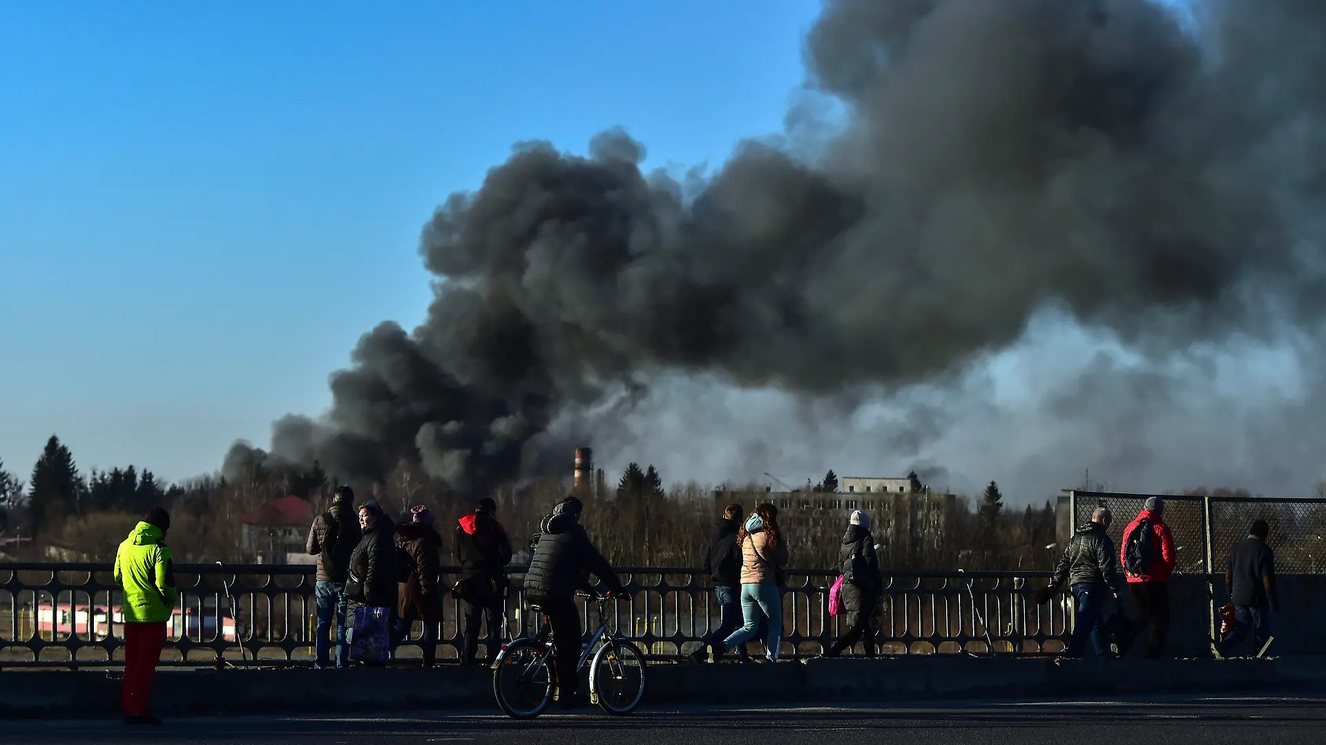 18.03.2022, Ukraine, Lwiw: Menschen stehen auf einer Überführung und schauen auf eine Rauchwolke, die nach einer Explosion in der Nähe des Flughafens aufsteigt. Am Flughafen der westukrainischen Großstadt Lwiw (Lemberg) haben sich am Morgen heftige Explosionen ereignet. Dort seien mehrere russische Raketen eingeschlagen, teilte Bürgermeister Sadowij auf Telegram mit. Foto: Ismail Coskun/IHA/AP/dpa +++ dpa-Bildfunk +++