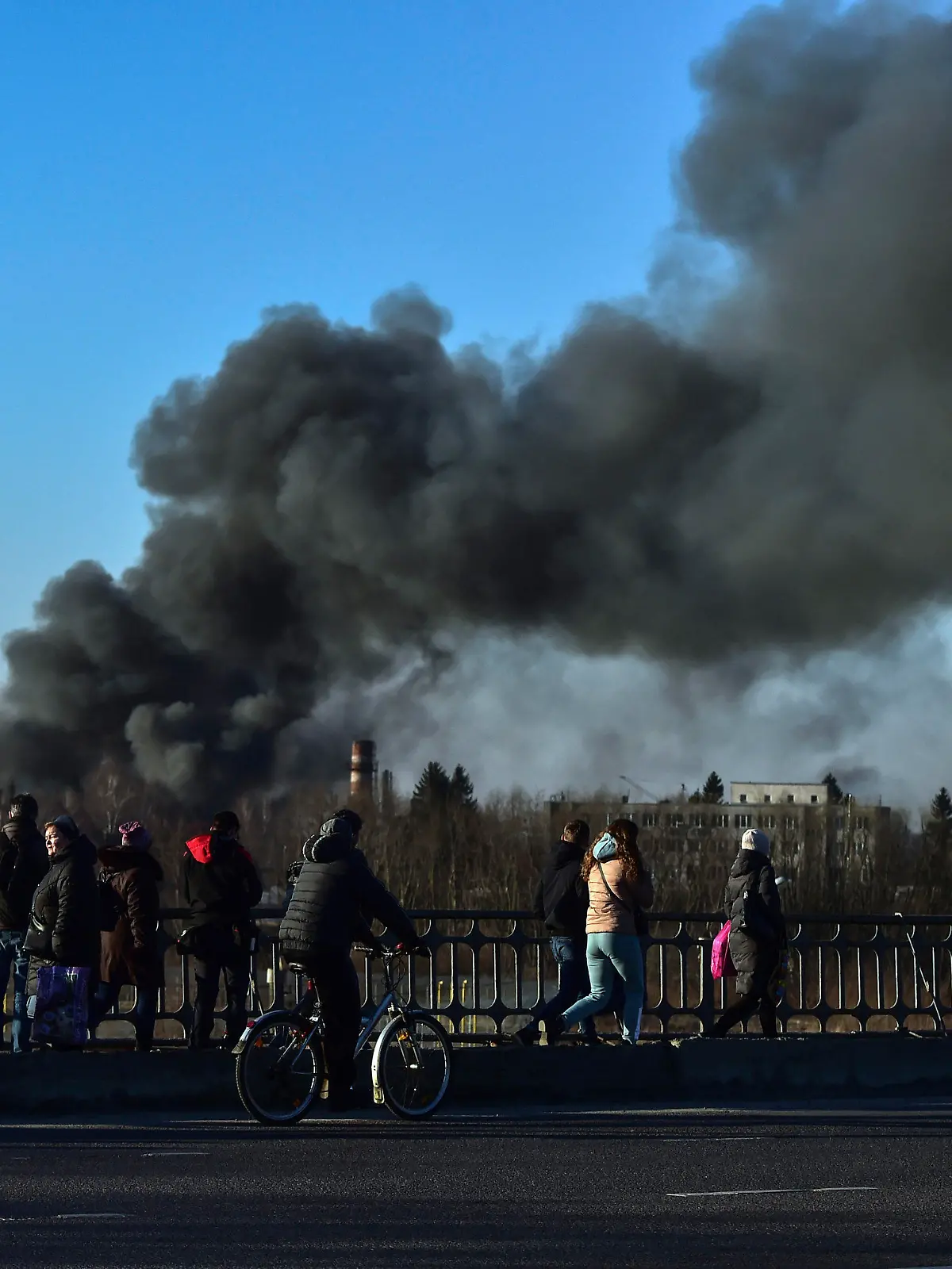 18.03.2022, Ukraine, Lwiw: Menschen stehen auf einer Überführung und schauen auf eine Rauchwolke, die nach einer Explosion in der Nähe des Flughafens aufsteigt. Am Flughafen der westukrainischen Großstadt Lwiw (Lemberg) haben sich am Morgen heftige Explosionen ereignet. Dort seien mehrere russische Raketen eingeschlagen, teilte Bürgermeister Sadowij auf Telegram mit. Foto: Ismail Coskun/IHA/AP/dpa +++ dpa-Bildfunk +++
