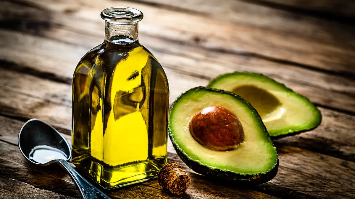 Vegan food: extra virgin avocado oil in a glass bottle shot on rustic wooden table. Sliced organic avocado and a spoon filled with oil are beside the bottle. Predominant colors are yellow and green. High resolution 42Mp studio digital capture taken with Sony A7rII and Sony FE 90mm f2.8 macro G OSS lens