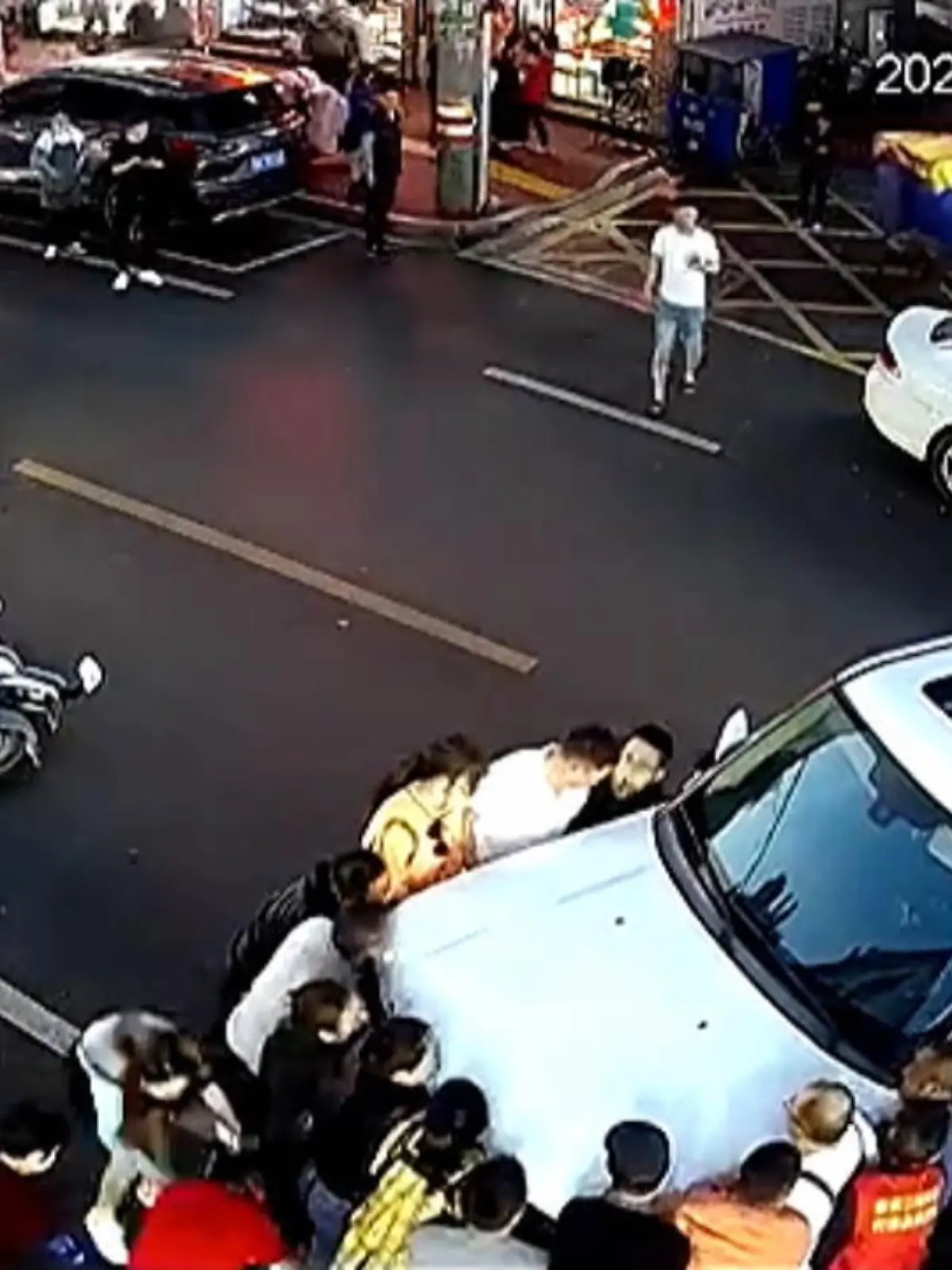 Ein kleines Mädchen fällt vom Roller und wird dann von einem Auto überrollt. Doch Anwohner eilen zur Hilfe und heben das Auto an.