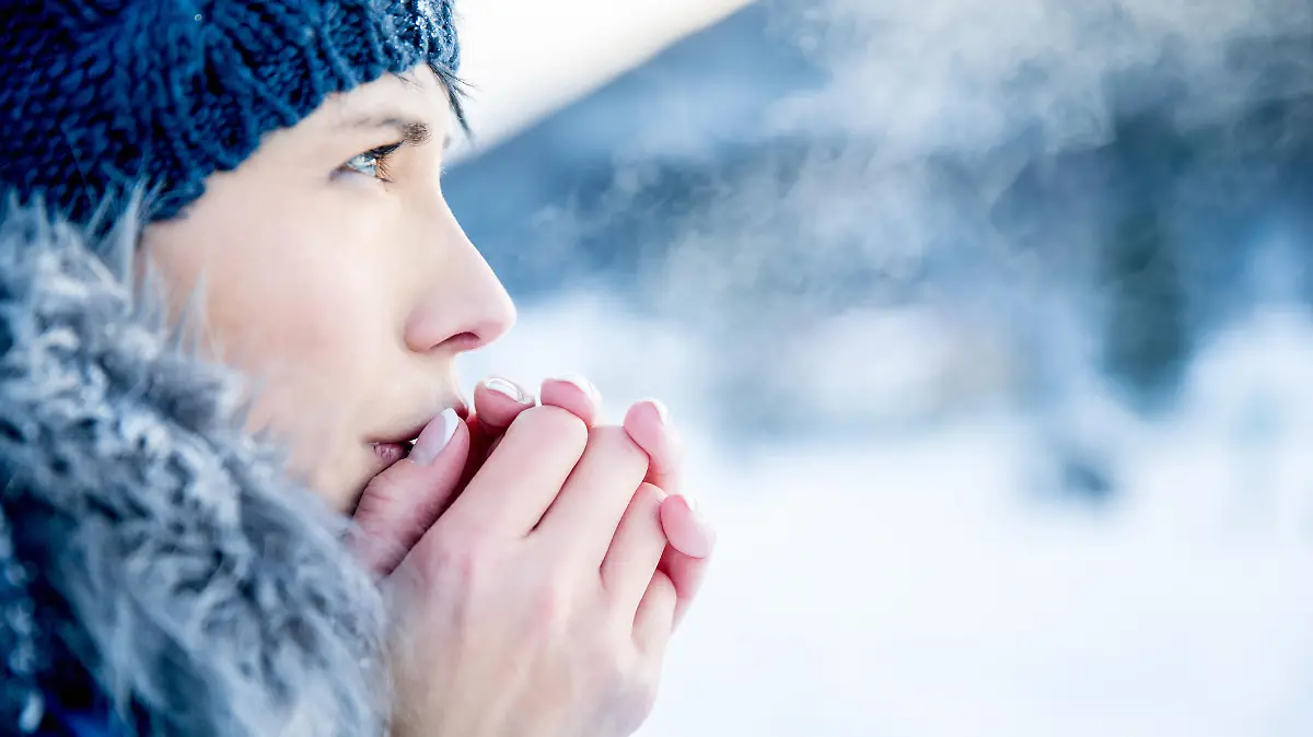 Young woman portrait on a cold winter day. Overcast and cold weather. She is heating her hands with her hot breath.
