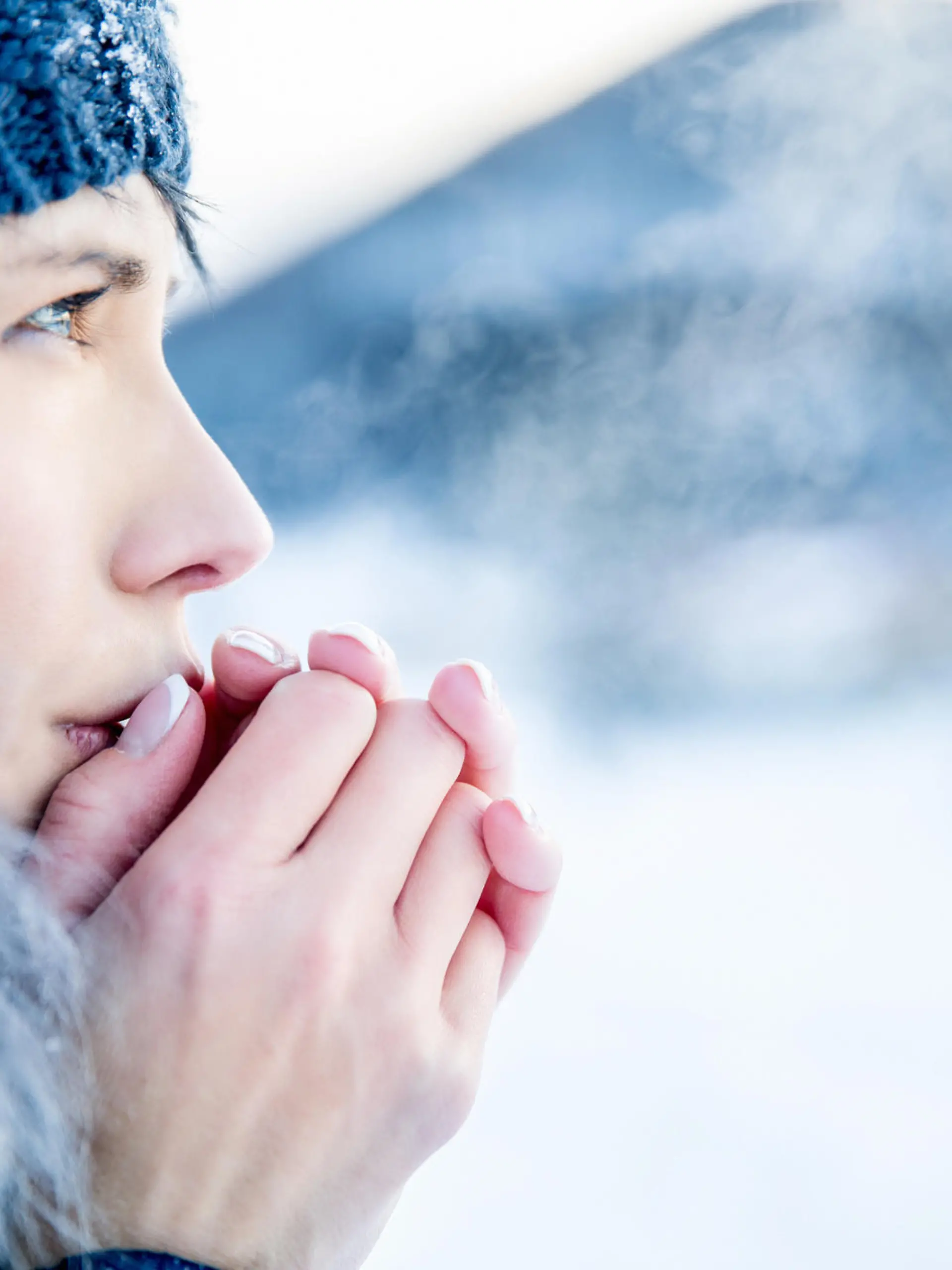 Young woman portrait on a cold winter day. Overcast and cold weather. She is heating her hands with her hot breath.
