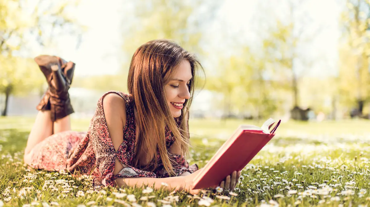 Young happy female student enjoying in spring day at the park and learning from a book.