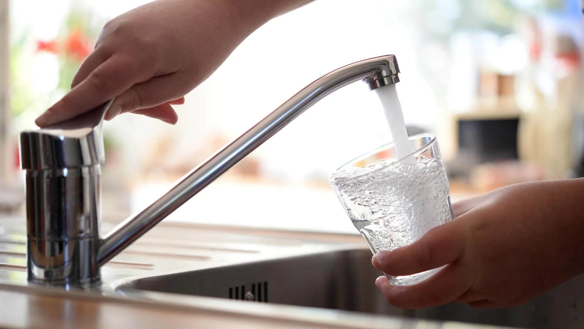 Frisches Leitungswasser fließt sprudelnd aus einem Wasserhahn in ein Glas