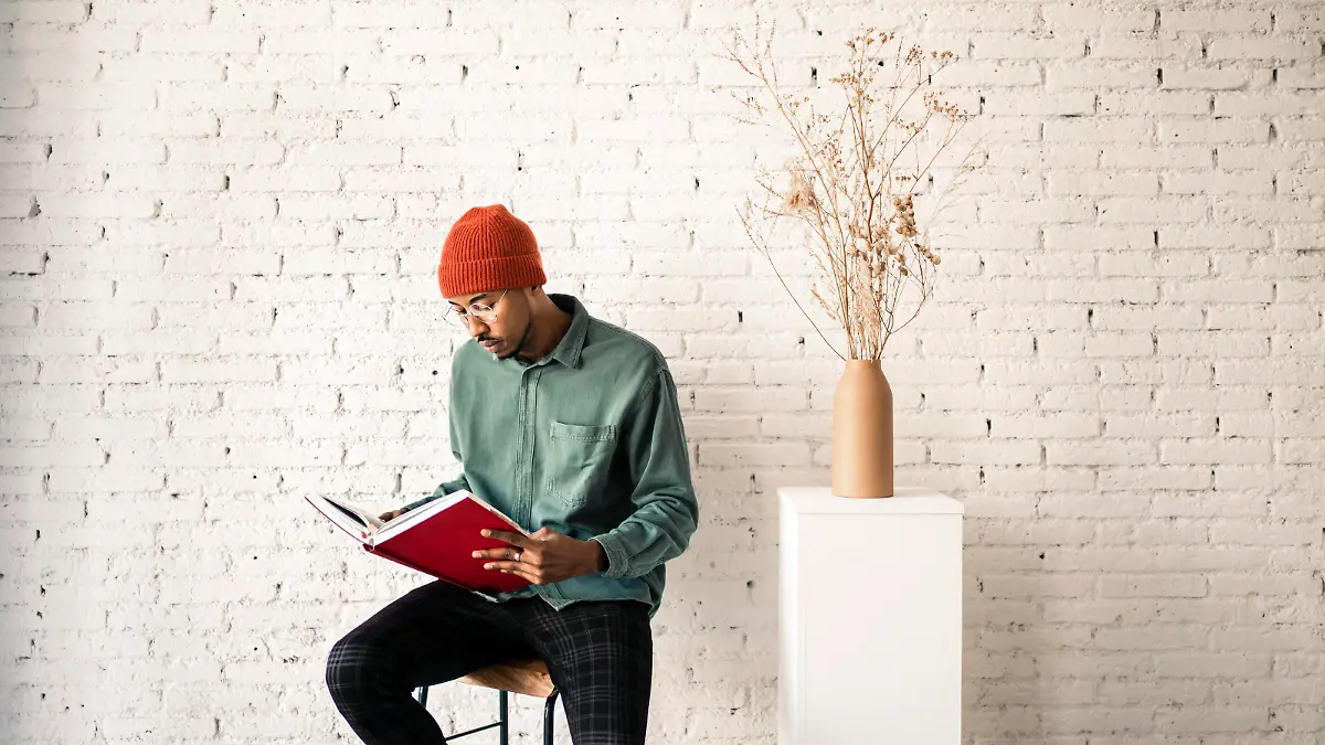 Man in knit hat reading book by dried plant vase against white brick wall model released Symbolfoto property released RCPF00507