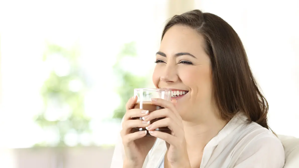Candid girl drinking cocoa shake sitting on a couch in the living room at home