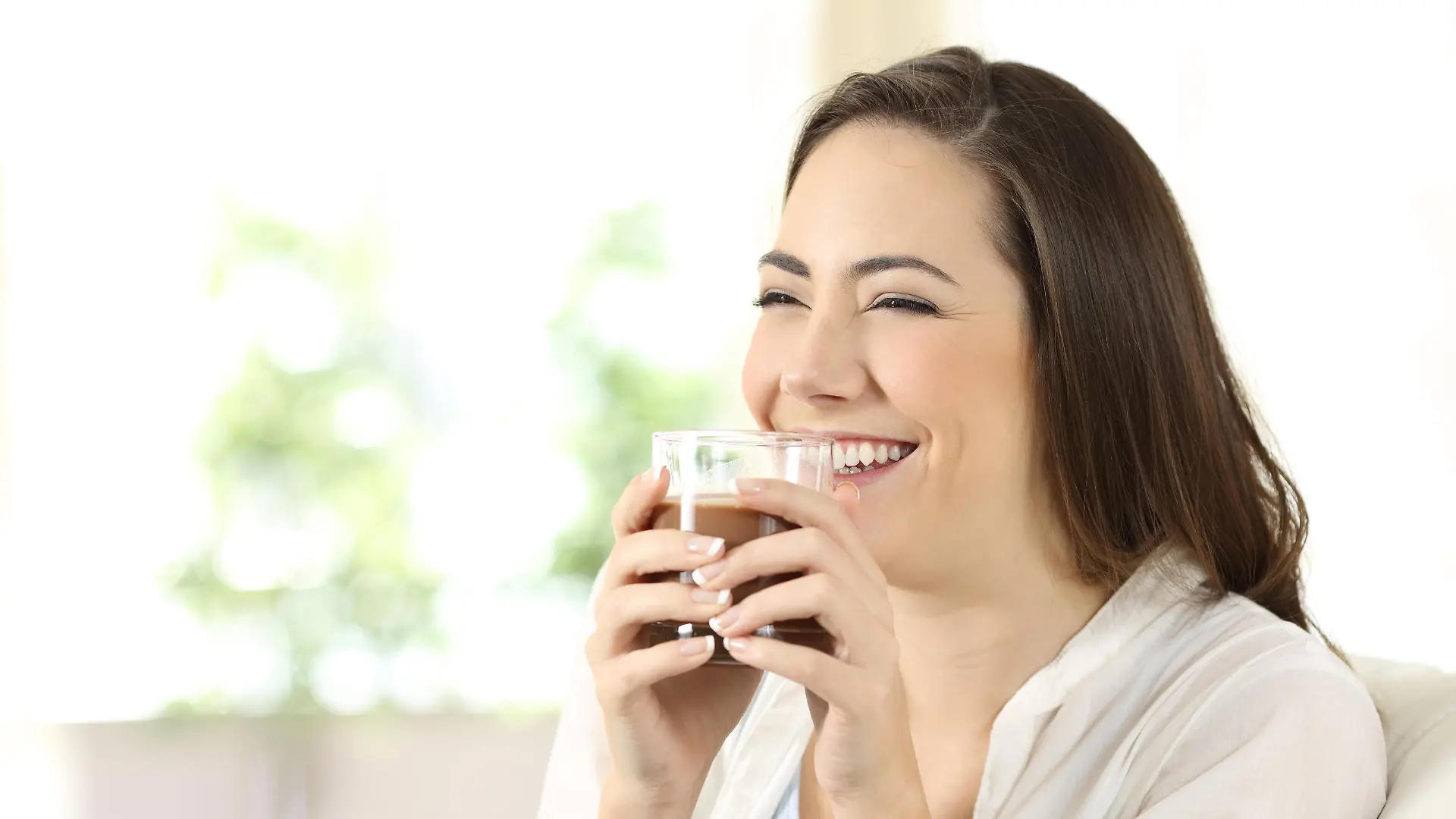 Candid girl drinking cocoa shake sitting on a couch in the living room at home
