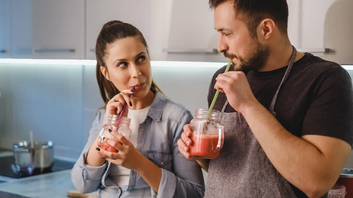 Couple flirting in the kitchen while drinking smoothie with a straw