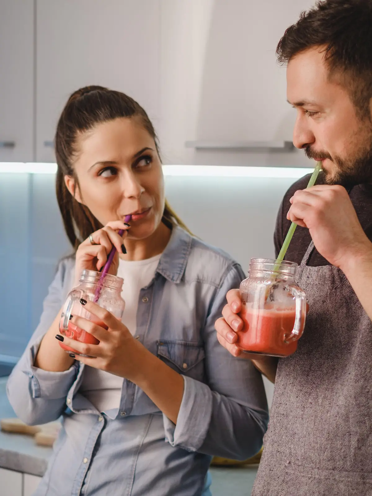 Couple flirting in the kitchen while drinking smoothie with a straw