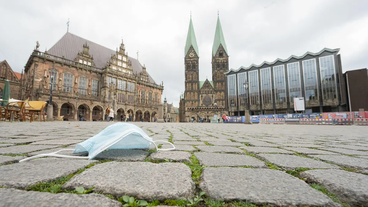 ILLUSTRATION - 11.10.2020, Bremen: Ein Mund-Nasen-Schutz liegt auf den Pflastersteinen vor dem Alten Rathaus (l-r), dem Bremer St.-Petri-Dom und der Bremischen Bürgerschaft. Foto: Mohssen Assanimoghaddam/dpa +++ dpa-Bildfunk +++