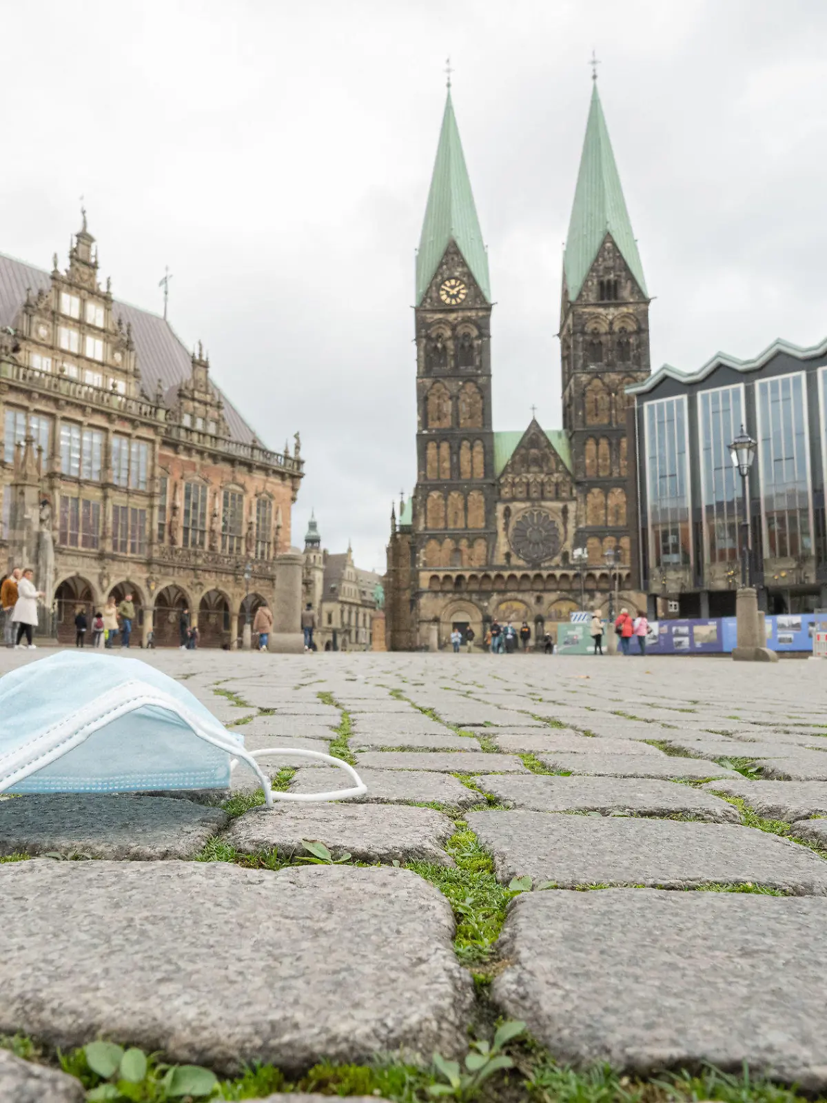 ILLUSTRATION - 11.10.2020, Bremen: Ein Mund-Nasen-Schutz liegt auf den Pflastersteinen vor dem Alten Rathaus (l-r), dem Bremer St.-Petri-Dom und der Bremischen Bürgerschaft. Foto: Mohssen Assanimoghaddam/dpa +++ dpa-Bildfunk +++