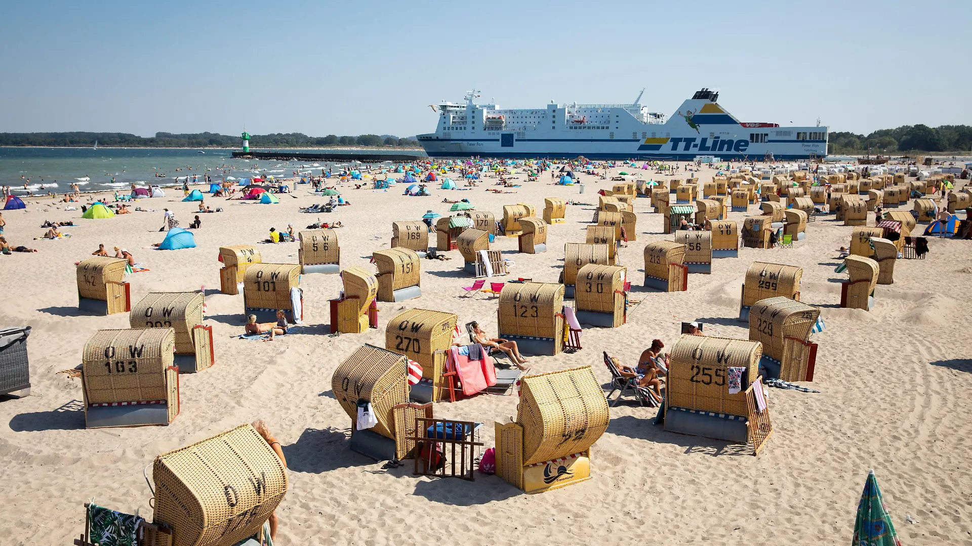 ARCHIV - 11.08.2020, Schleswig-Holstein, Travemünde: Urlauber und Tagesgäste verbringen bei strahlendem Sonnenschein und warmen Temperaturen den Tag am Strand von Travemünde, während im Hintergrund eine Fähre der TT-Line ausläuft. Der «Corona-Sommer» 2020 hat in vielen Tourismusorten in Schleswig-Holstein einen weniger großen Schaden angerichtet, als zunächst befürchtet. Foto: Christian Charisius/dpa - ACHTUNG: Verwendung nur im vollen Format +++ dpa-Bildfunk +++