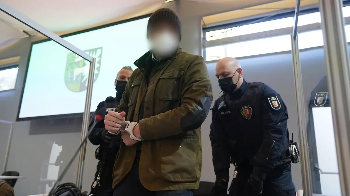 07.03.2022, Schleswig-Holstein, Kiel: Justizbeamte bringen den Angeklagten (M) in Handschellen in den Sitzungssaal der Außenstelle des Landgerichts Kiel zu Beginn des Prozesstages wegen eines Dreifachmordes. Am 19. Mai 2021 soll der Mann zuerst seine von ihm getrennt lebende Ehefrau und deren neuen Bekannten in Dänischenhagen mit einer Maschinenpistole erschossen und danach in Kiel einen gemeinsamen Bekannten des Ehepaares mit einer halbautomatischen Pistole getötet haben. Mit der zweiten Waffe stellte er sich am Abend in Hamburg der Polizei. Foto: Marcus Brandt/dpa - ACHTUNG: Der Angeklagte wurde aus rechtlichen Gründen gepixelt +++ dpa-Bildfunk +++