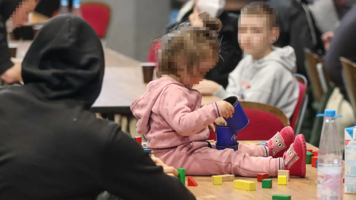 15.03.2022, Hessen, Alsfeld: Ein kleines Mädchen spielt auf einem Tisch in der zur Notunterkunft für Geflüchtete aus der Ukraine umfunktionierten Hessenhalle in Alsfeld. In der Stadt im Vogelsbergkreis befindet sich eine der vier Notunterkünfte für bis zu 1000 Menschen, mit deren Einrichtung das Land Hessen die Landkreise Marburg-Biedenkopf, Wetterau, Vogelsberg und Hochtaunus beauftragt hatte. Foto: Nadine Weigel/dpa - ACHTUNG: Person(en) wurde(n) aus rechtlichen Gründen gepixelt +++ dpa-Bildfunk +++