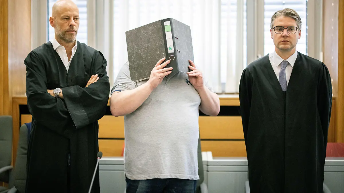 12.08.2020, Nordrhein-Westfalen, Essen: Der Angeklagte (M) steht zu Beginn des Prozesses im Gerichtssaal des Landgerichts mit einem Aktenordner vor dem Gesicht zwischen seinen Anwälten Stefan Tierel (l) und Leonhardt Mühlenfeld. Der 47 Jahre alte Mann aus Krefeld soll eine Bekannte im Juni 2019 mit einer über den Kopf gezogenen Plastiktüte erstickt haben. Hintergrund der Tat soll Eifersucht gewesen sein. Angeblich wollte sich die Frau von ihm trennen. Die Leiche ist bis heute nicht gefunden worden. Foto: Marcel Kusch/dpa - ACHTUNG: Schrift auf Ordnerrücken wurde aus rechtlichen Gründen gepixelt +++ dpa-Bildfunk +++