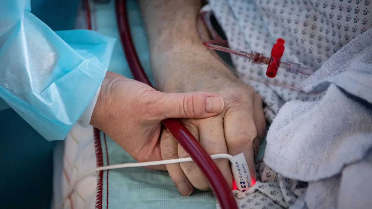 PRODUKTION - 16.02.2022, Hessen, Fulda: Eine Krankenschwester versorgt einen schwer an Corona erkrankten Patienten auf der Intensivstation des Klinikums in Fulda und hält dabei die Hand des Mannes. Viele Patienten mit schweren Verläufen liegen mehrere Wochen auf der Intensivstation, rund die Hälfte der künstlich beatmeten Patienten stirbt. (zu dpa "Sorgen um Engpässe in Kliniken und Altenheimen wegen Impfpflicht") Foto: Boris Roessler/dpa +++ dpa-Bildfunk +++