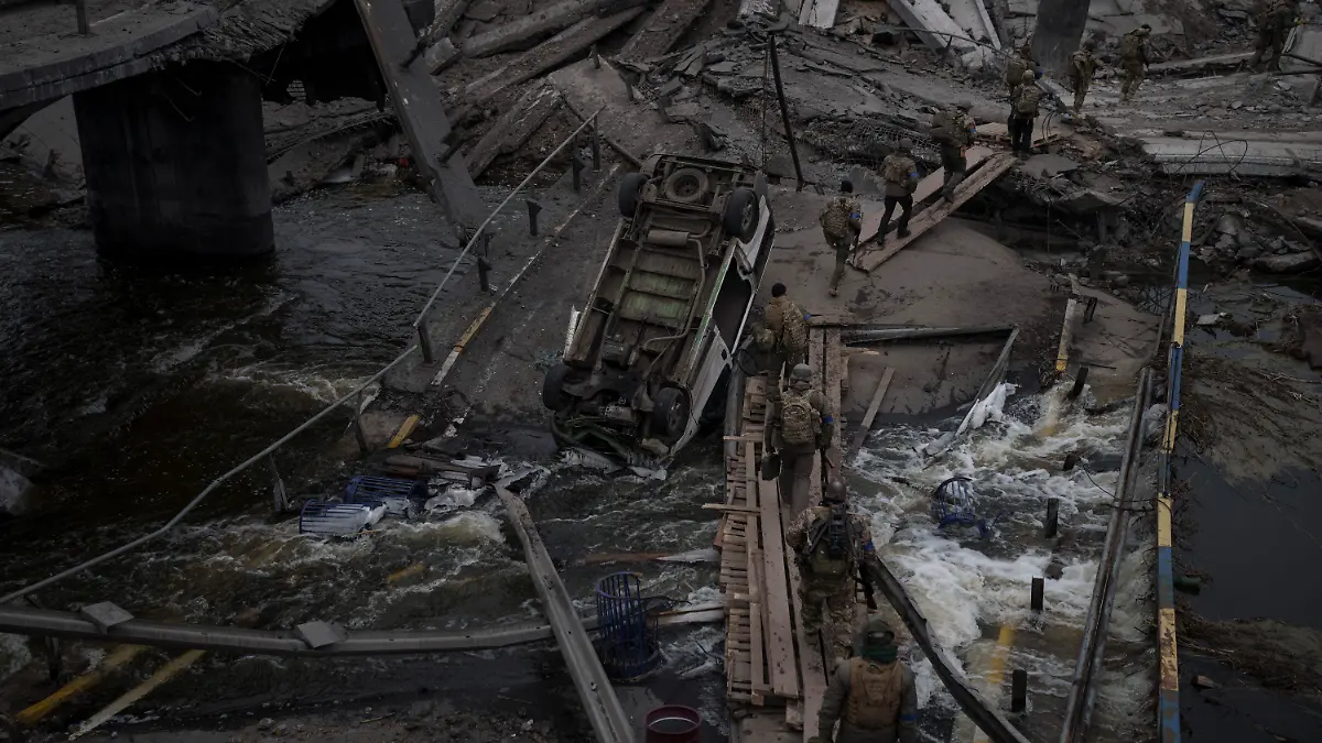 12.03.2022, Ukraine, Kiew: Ausländische und ukrainische Soldaten überqueren einen improvisierten Weg unter einer zerstörten Brücke in Irpin nordwestlich von Kiew. Die Bevölkerung von Städten und Dörfern in der Ukraine ist erneut unter verstärkten Beschuss der russischen Armee geraten. Foto: Felipe Dana/AP/dpa +++ dpa-Bildfunk +++