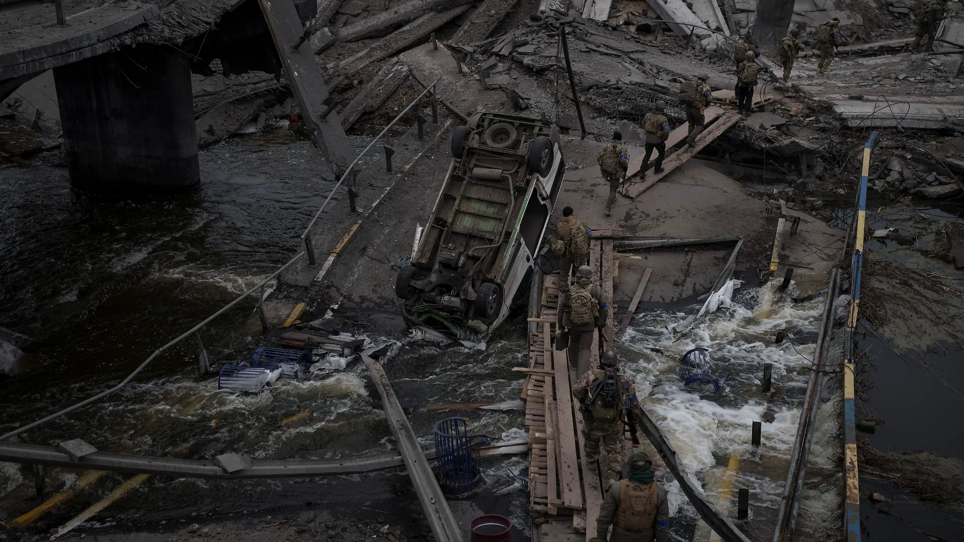 12.03.2022, Ukraine, Kiew: Ausländische und ukrainische Soldaten überqueren einen improvisierten Weg unter einer zerstörten Brücke in Irpin nordwestlich von Kiew. Die Bevölkerung von Städten und Dörfern in der Ukraine ist erneut unter verstärkten Beschuss der russischen Armee geraten. Foto: Felipe Dana/AP/dpa +++ dpa-Bildfunk +++