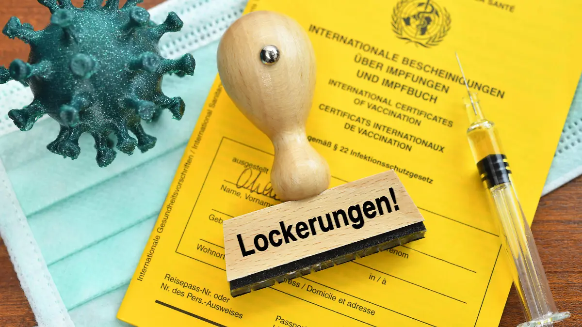 FOTOMONTAGE, Impfpass, Coronavirus-Modell, Impfspritze und Stempel mit der Aufschrift Lockerungen *** PHOTOMONTAGE, vaccination certificate, coronavirus model, vaccination syringe and stamp with the inscription relaxations