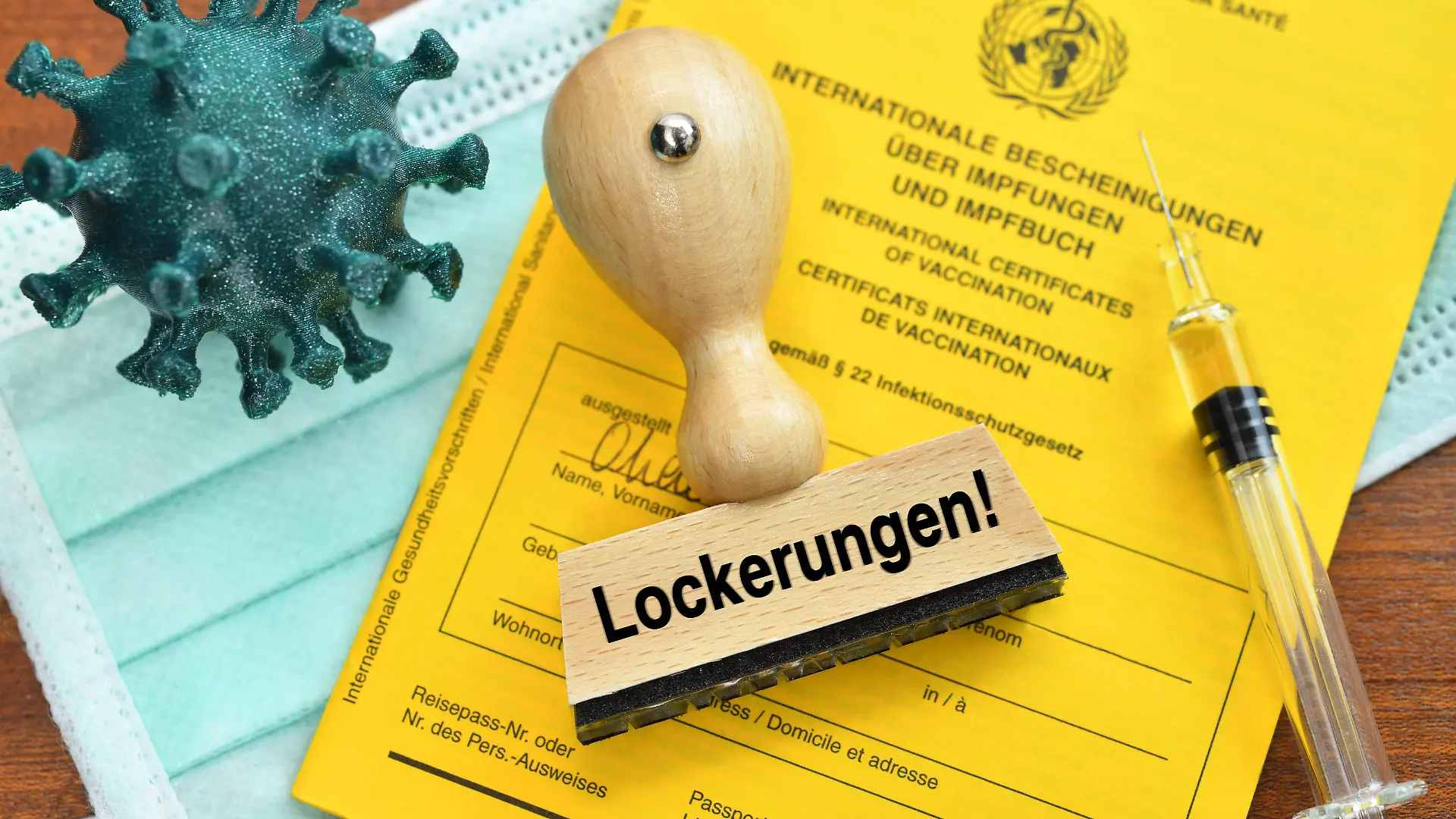 FOTOMONTAGE, Impfpass, Coronavirus-Modell, Impfspritze und Stempel mit der Aufschrift Lockerungen *** PHOTOMONTAGE, vaccination certificate, coronavirus model, vaccination syringe and stamp with the inscription relaxations