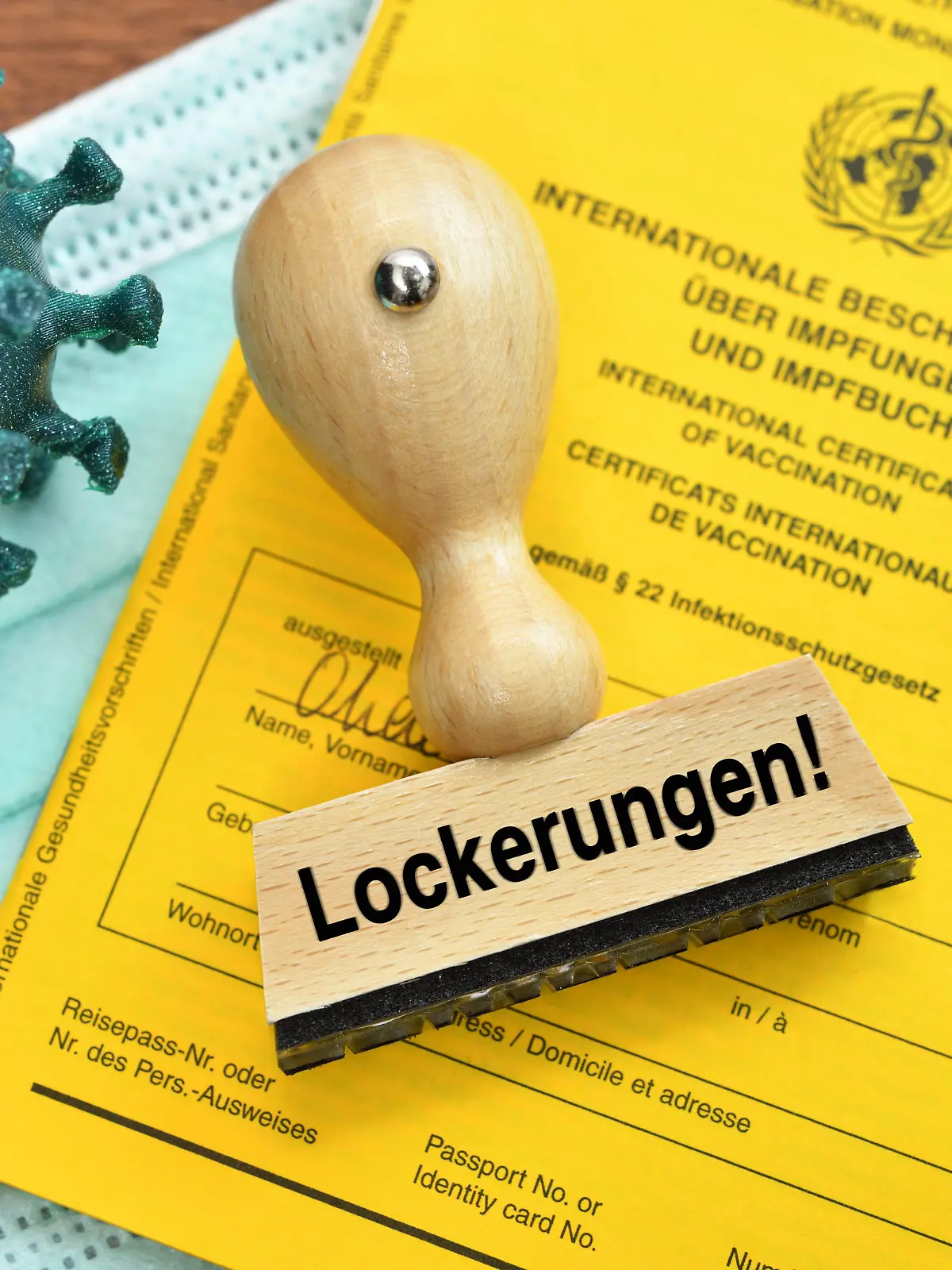FOTOMONTAGE, Impfpass, Coronavirus-Modell, Impfspritze und Stempel mit der Aufschrift Lockerungen *** PHOTOMONTAGE, vaccination certificate, coronavirus model, vaccination syringe and stamp with the inscription relaxations 