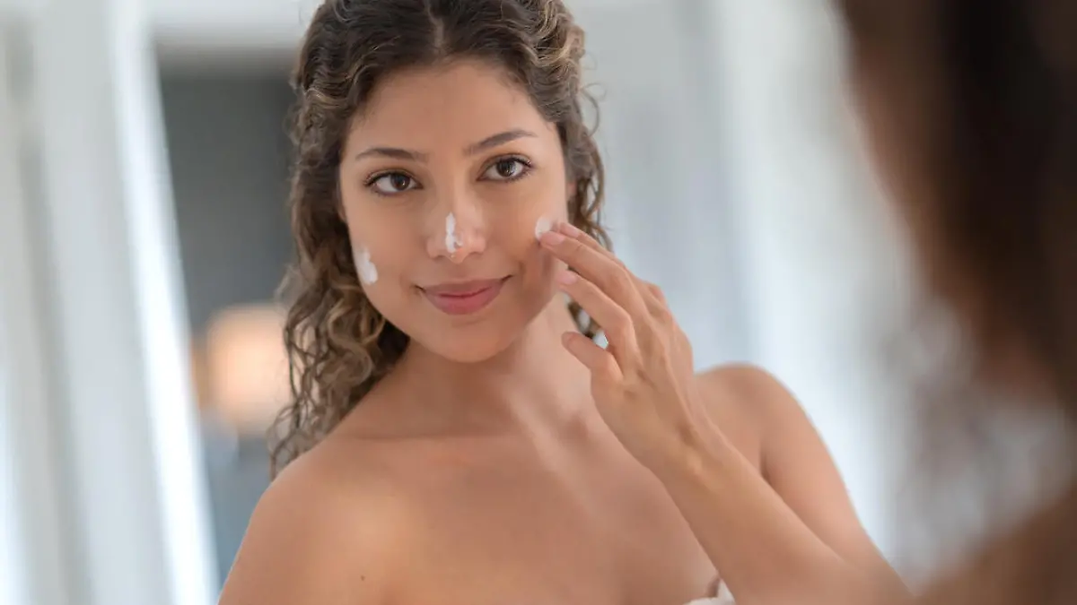 Portrait of a beautiful woman in the bathroom applying moisturizer on her face and looking in the mirror