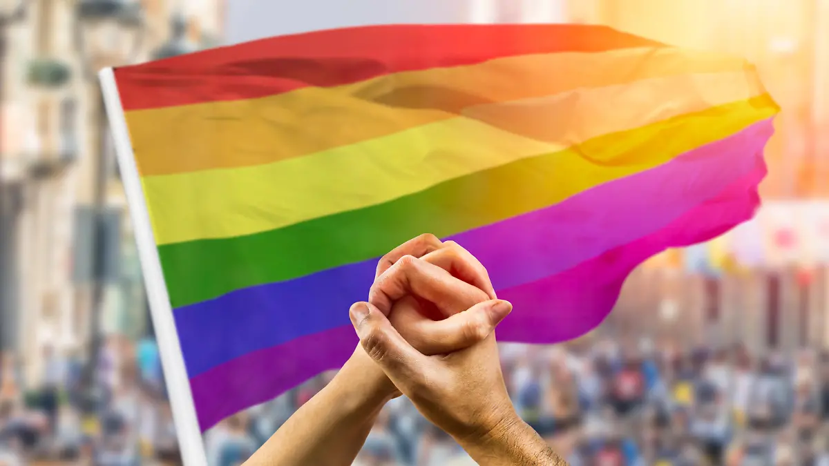 Ein homosexuelles Paar hält Händchen, im Hintergrund sieht man die Regenbogen-Flagge, die für die LGBT-Community steht.