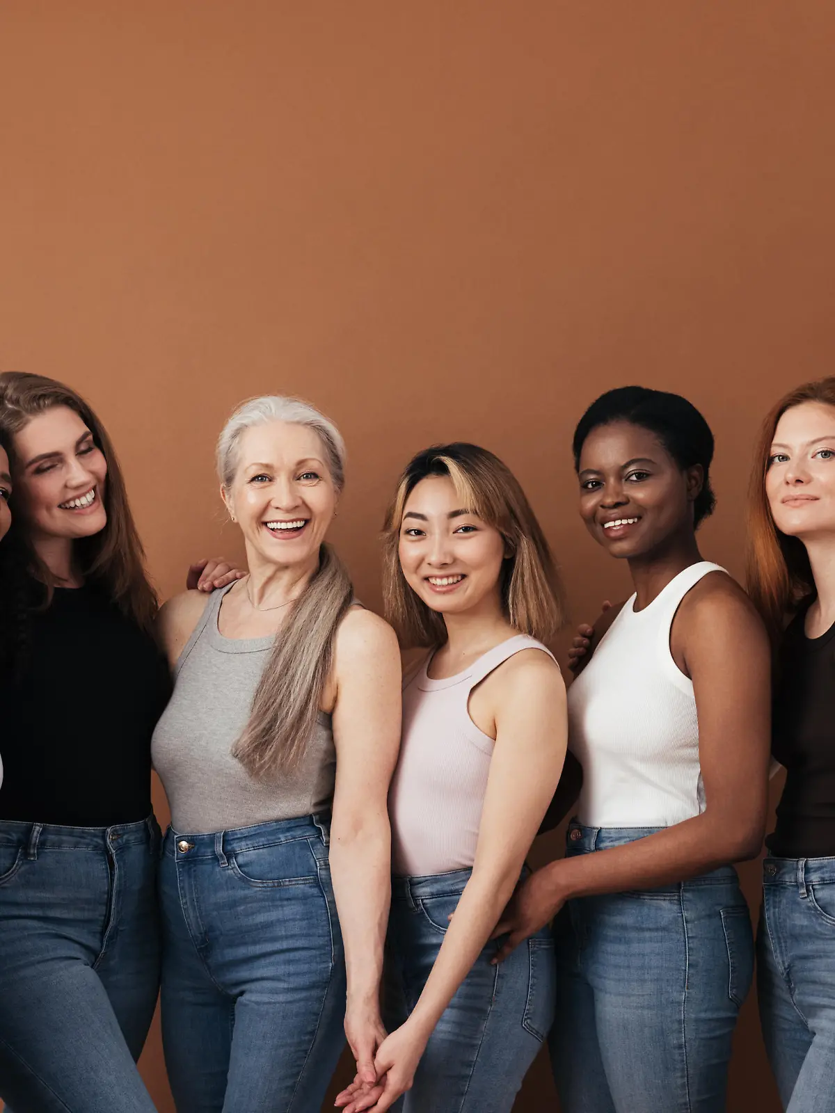Multi-ethnic group of women of different ages posing against brown background looking at camera
