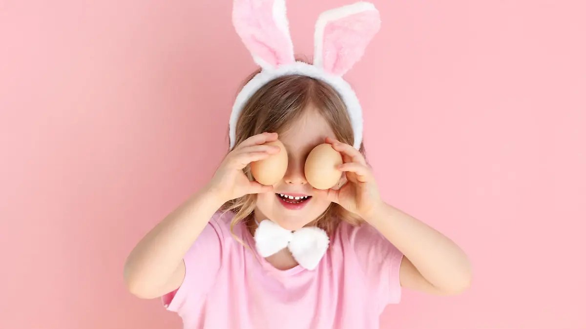 Cute little child wearing bunny ears holding egg on Easter day . Easter girl portrait, funny emotions, surprise. Copyspace for text.